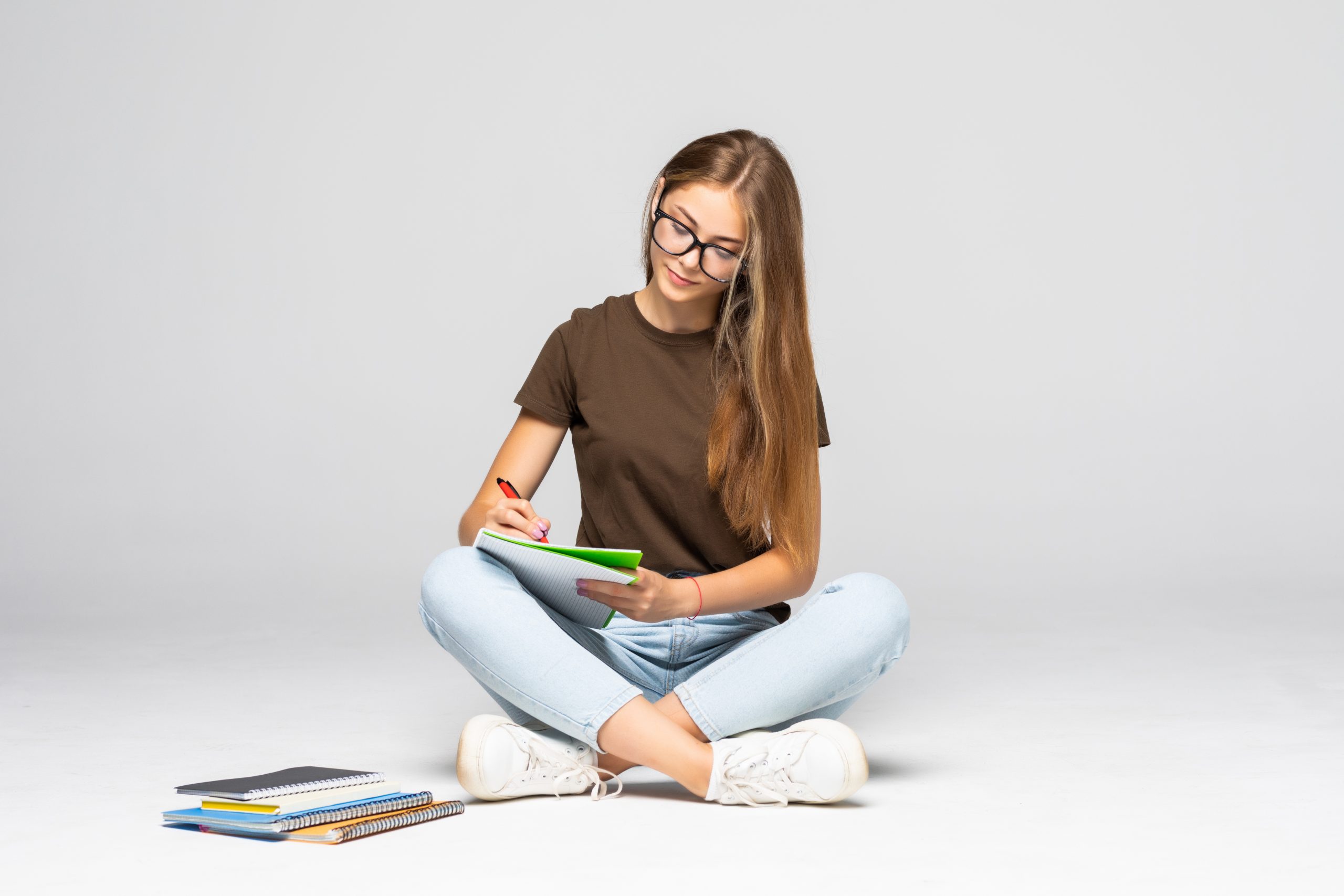 smiling young casual woman writing on her notepad while sitting on white background